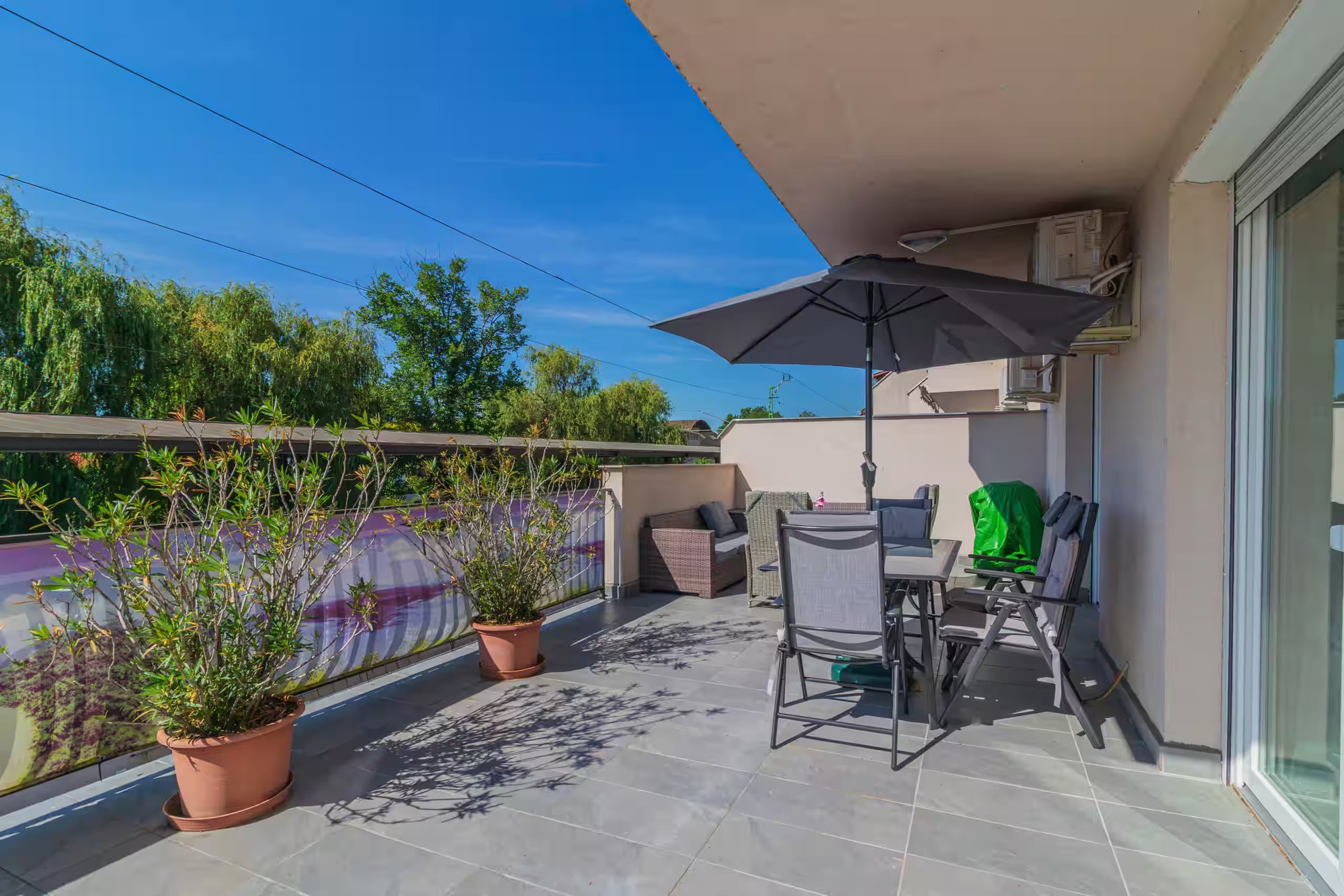 Großzügige Terrasse mit Pflanzen, Sonnenschirm und Esstisch